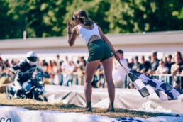 Woman with the chequered flag standing on straw bales as a rider approaches at Glemseck 101