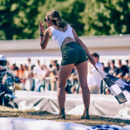 Woman with the chequered flag standing on straw bales as a rider approaches at Glemseck 101