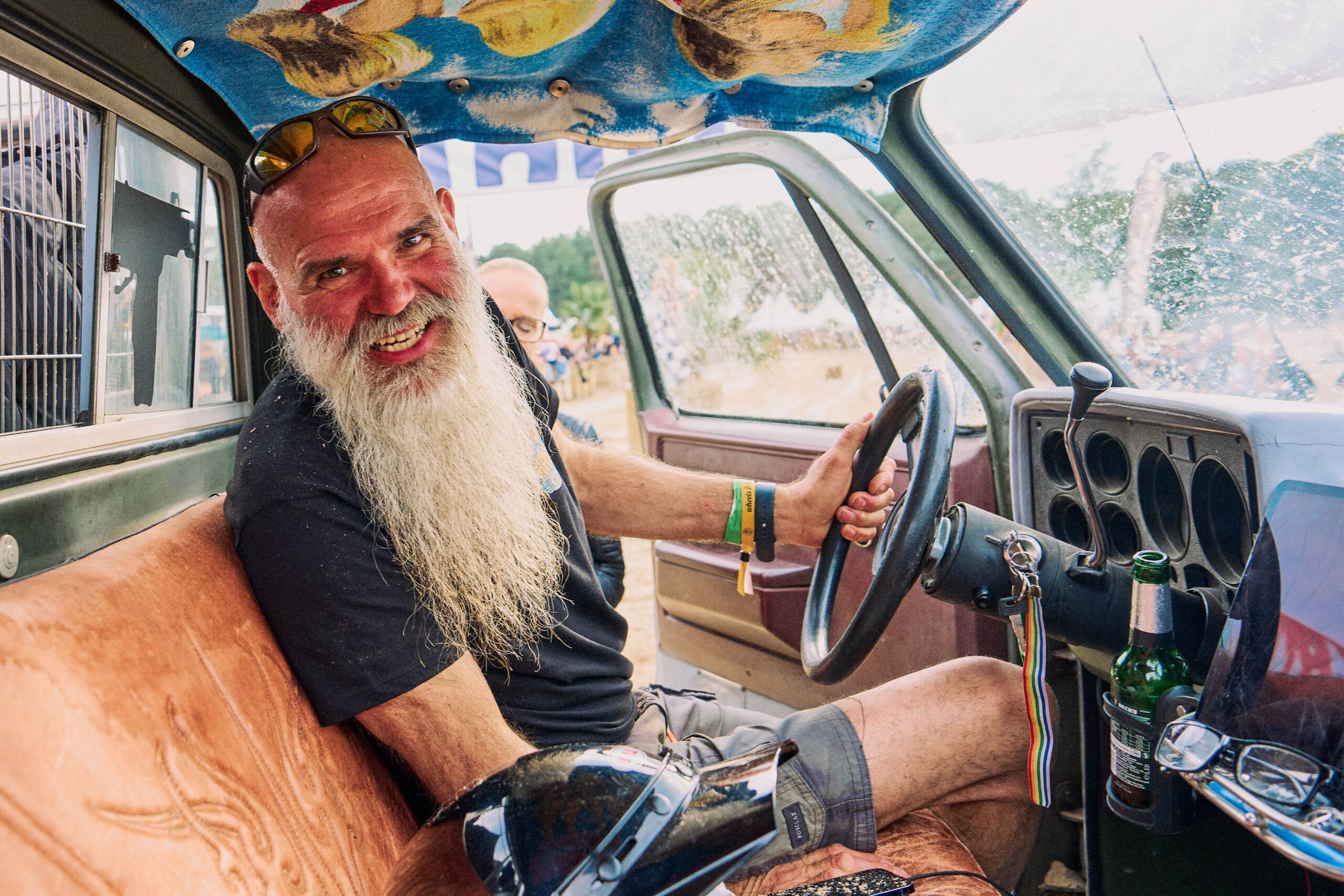 Smiling man with a long white beard behind the wheel of an old car with a painted headliner at Wheels and Wake
